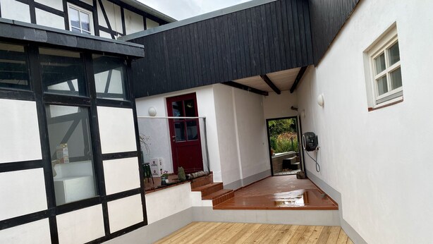 A modern building with a wooden deck, a red door, and a small garden area. - Eichhaus Eifel (Rheinbach)