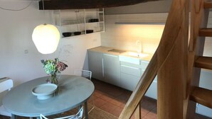 A compact kitchen with white cabinets, a round table with a bowl and flowers, and a wooden staircase. - Eichhaus Eifel (Rheinbach)