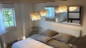 A bedroom with a bed, a chair, a large mirror, and a window with curtains. - Eichhaus Eifel (Rheinbach)