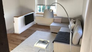 A living room with a sofa, a TV, a lamp, and a window with blinds. - Eichhaus Eifel (Rheinbach)
