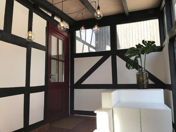 A room with exposed wooden beams, a white bench, a potted plant, and hanging light fixtures.