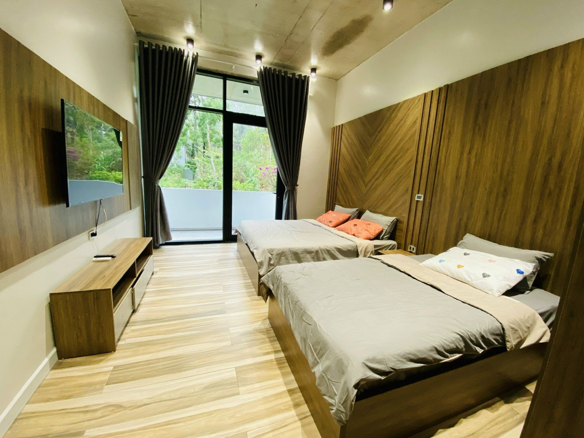 A modern bedroom with two beds, a TV, and a balcony with curtains.