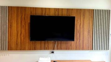 A modern living room with a flat-screen TV mounted on a wooden panel wall, a wooden entertainment unit with drawers, and a wooden floor.