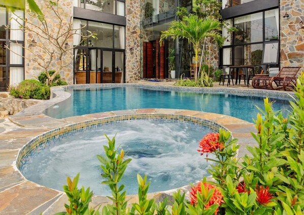 Una piscina con hidromasaje, rodeada de muros de piedra y abundante vegetación.