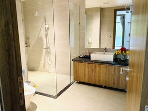 Un baño moderno con ducha acristalada, tocador de madera y un espejo grande.