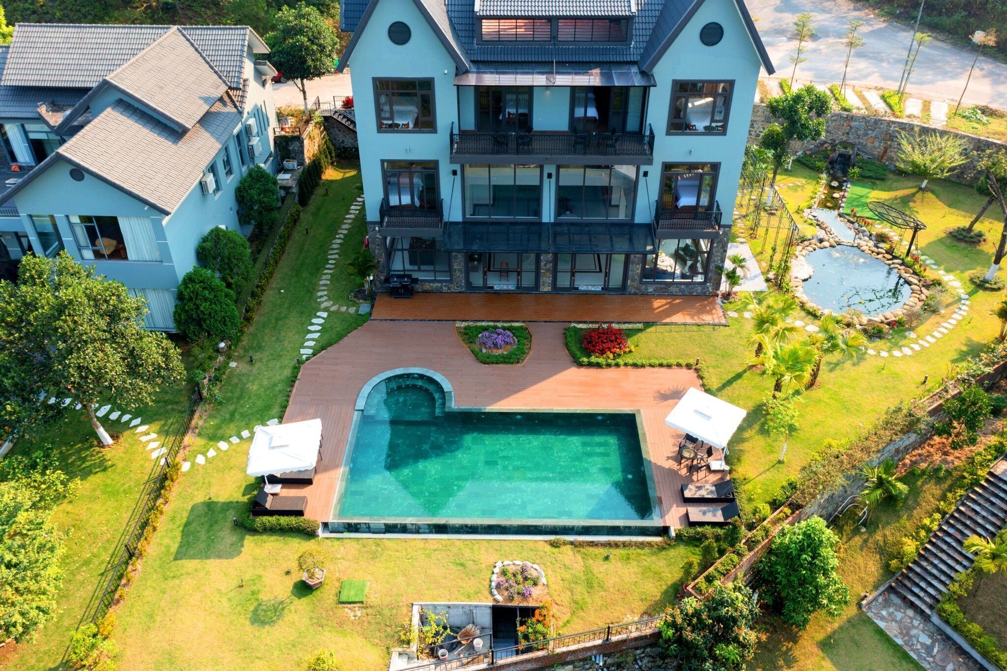 Une grande maison à deux étages avec une piscine, entourée d’un jardin bien entretenu et d’un chemin en pierre.