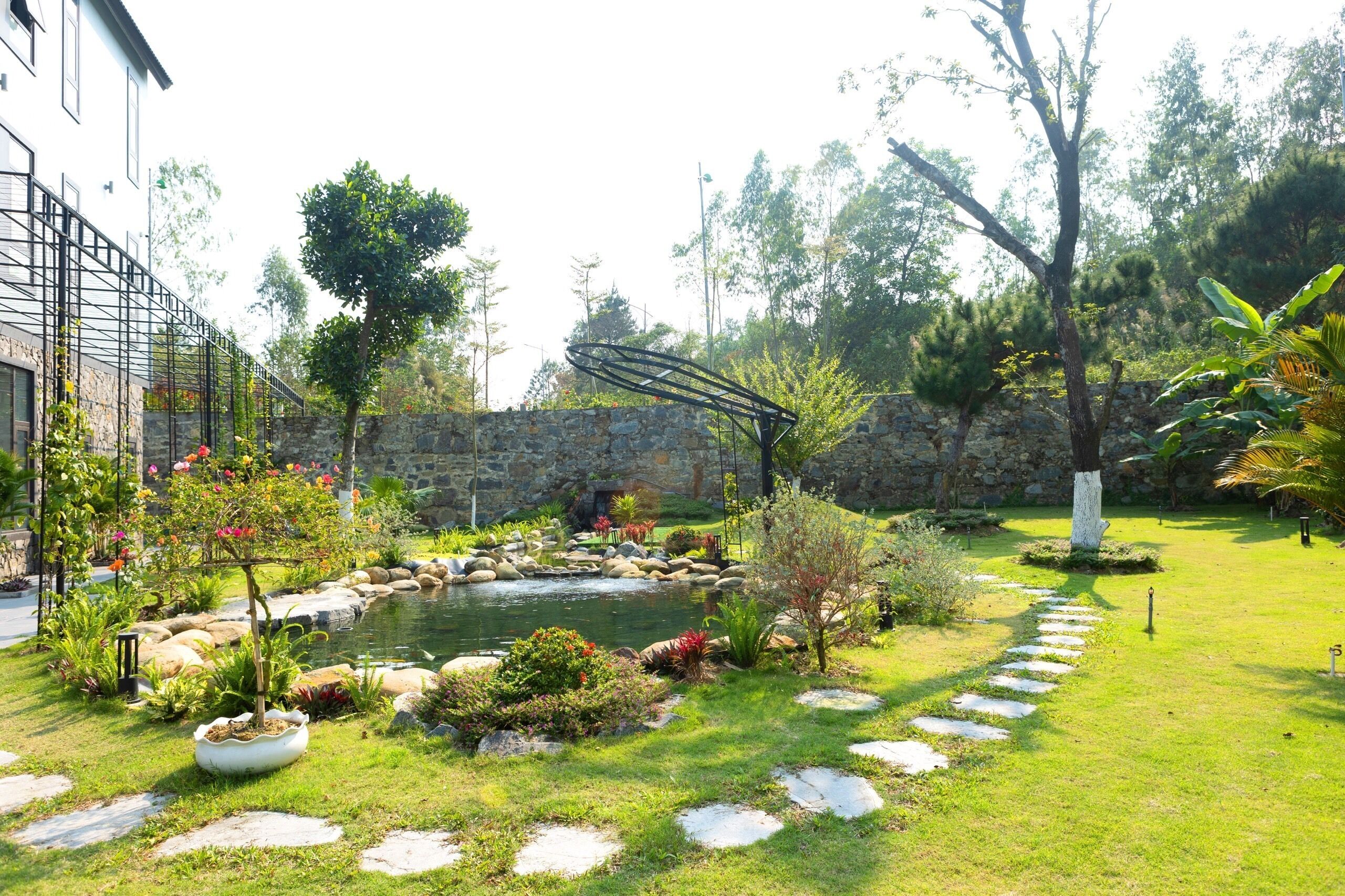 Ein Garten mit Teich, Steinmauern und einer Metallskulptur.