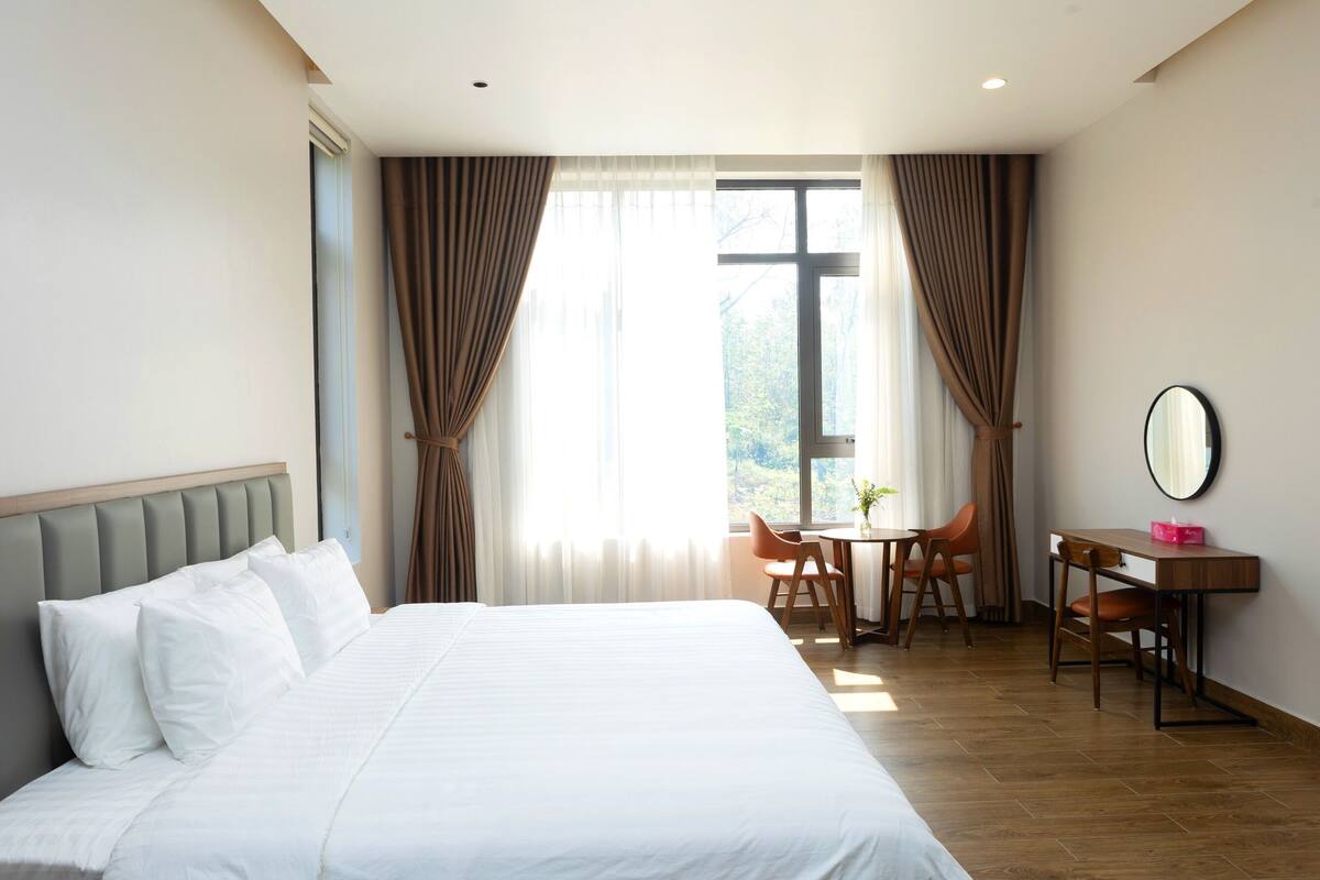 Ein Hotelzimmer mit einem großen Bett, einem Schreibtisch mit Stuhl und einem Vorhangfenster.