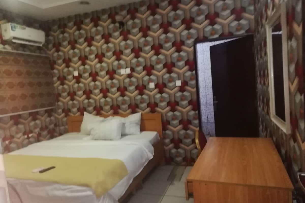 Een slaapkamer met een behang, een bed met witte lakens, een nachtkastje en een airconditioning.