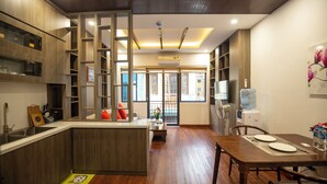 A modern kitchen with wooden cabinetry, a central island, and a dining area with a table and chairs. - Sumitomo 11 APT - Alley 39 Linh lang (Hanoi)