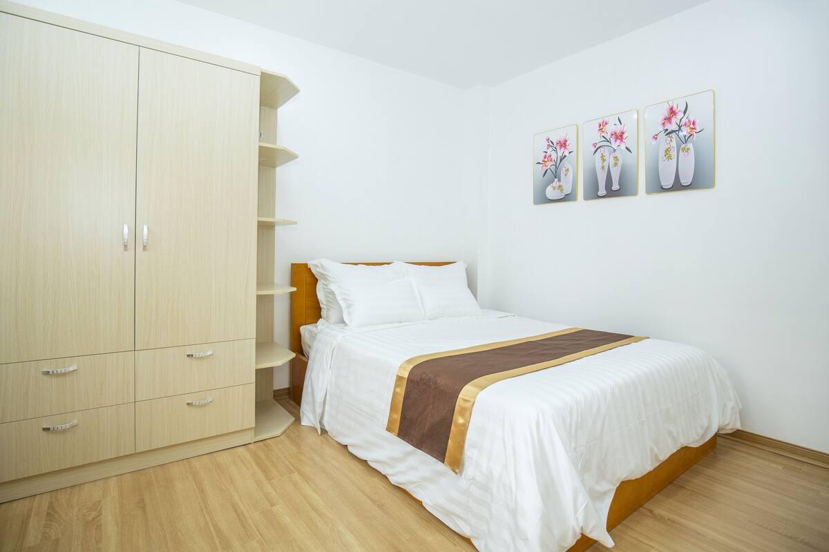 A bedroom with a bed, a wardrobe, and three wall-mounted flower paintings.