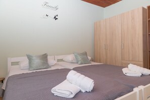 Een net opgemaakt bed met een grijze spreidek en witte kussens, een houten garderobe en een muur met een 'Family' bord.