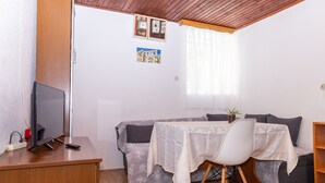 Una habitación acogedora con techo de madera, un sofá gris, una pequeña mesa de comedor con mantel blanco, una silla blanca y un televisor sobre un escritorio de madera.