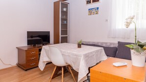 Una sala pequeña con televisor, aparador, sofá y una mesa con control remoto.