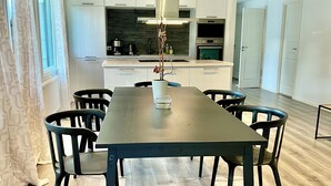 Ein zeitgemäßer Essbereich mit einem Holztisch und Stühlen, einer weißen Vase mit Pflanze sowie einer Küche im Hintergrund.