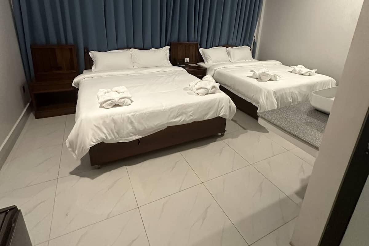 Habitación de hotel con dos camas, una mesita de noche de madera, una cortina azul y suelo de baldosas.