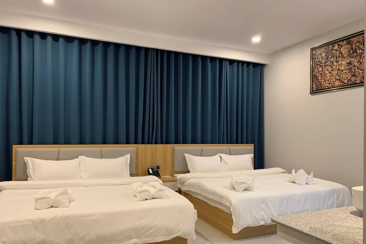 Habitación de hotel con dos camas, una cortina azul grande, cabecero de madera, ropa de cama blanca y una mesita de noche pequeña con un teléfono.