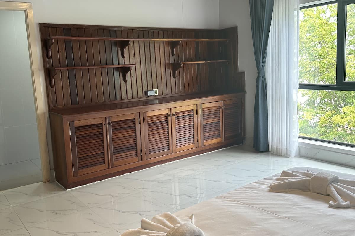 Habitación de hotel con techo de madera, una cama grande con toallas, un armario de madera y una ventana con vistas a árboles.