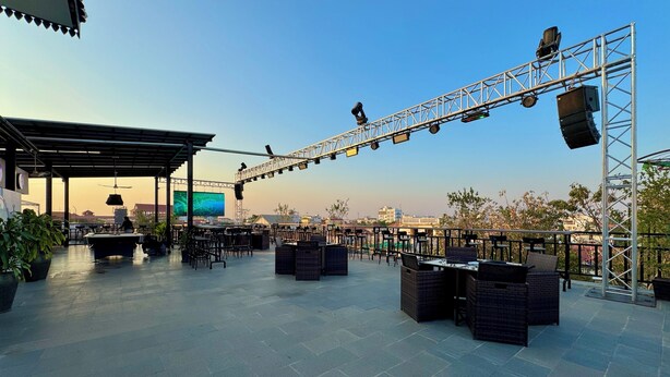 Een terras met tafels en stoelen, een podium met verlichting, en een uitzicht op de skyline van de stad.