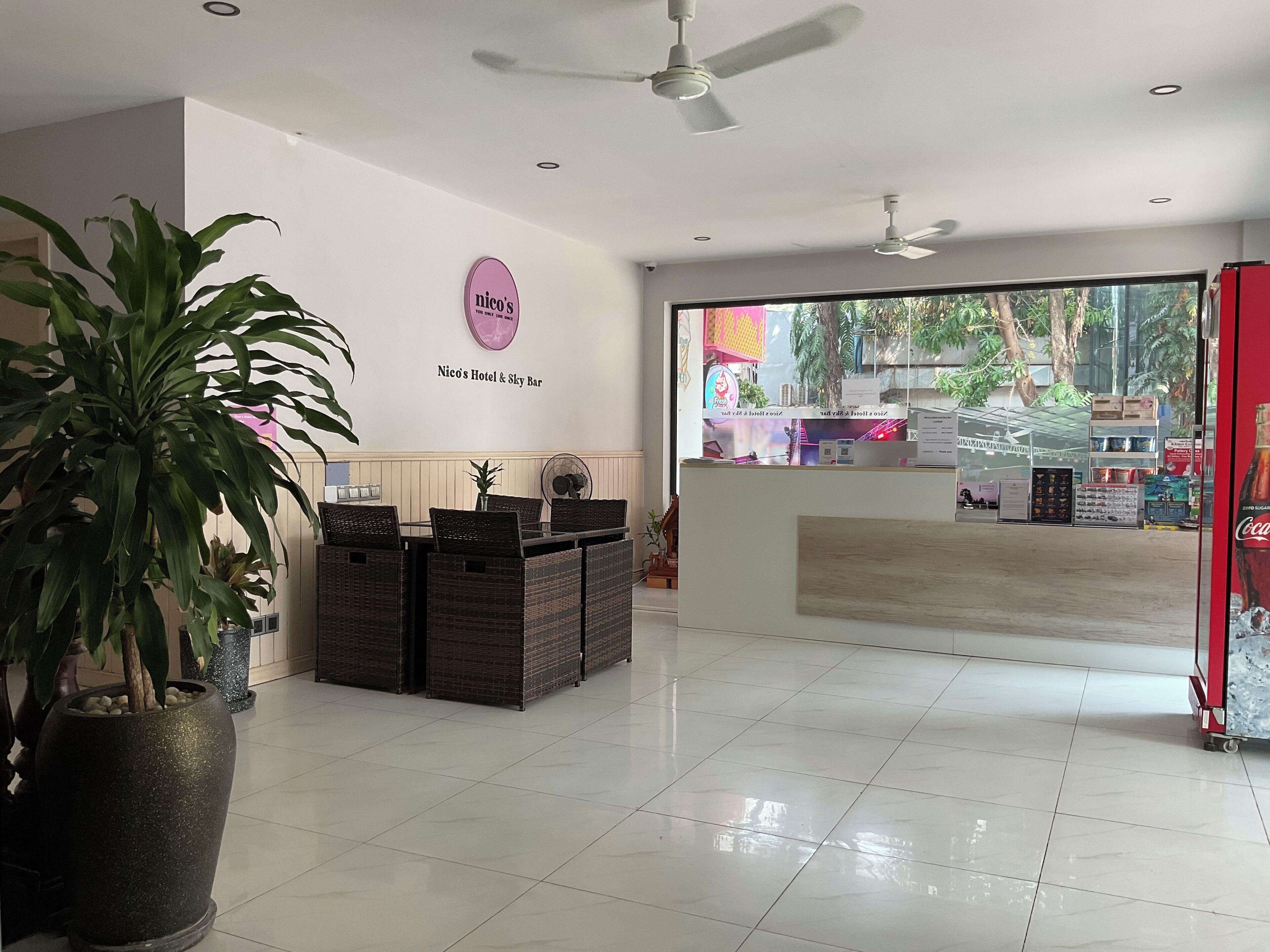 A reception area with a sign for 'Nico's Hotel & Sky Bar', a reception desk, and a large window offering a view of the outside.