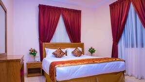 A neatly arranged bedroom with a wooden bed, red curtains, a bedside table with a vase of flowers, and a nightstand. - Sara Furnished Apartments (Al Khobar)