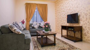 A living room with a sofa, a coffee table, a TV stand, and a floral-patterned wall. - Sara Furnished Apartments (Al Khobar)