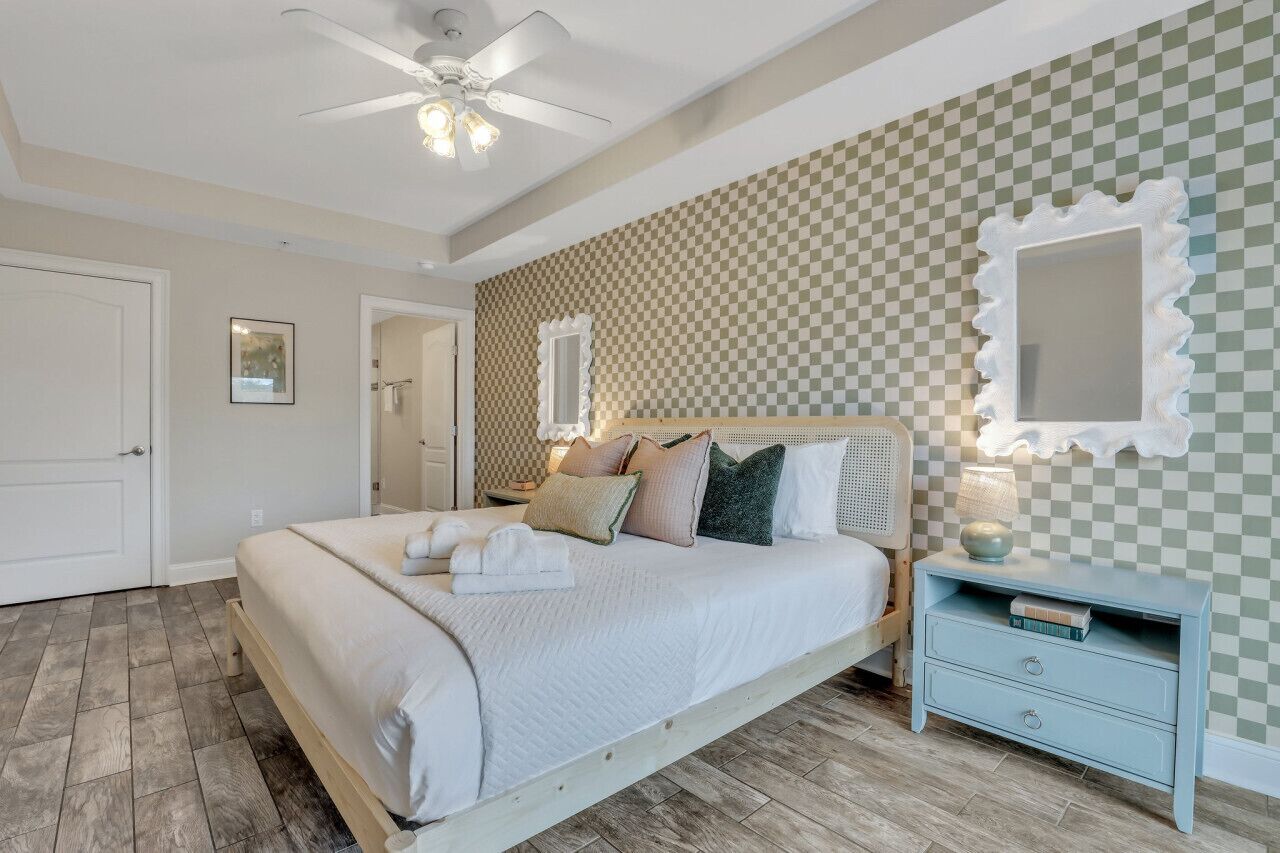 A bedroom with a bed, a nightstand, a ceiling fan, and a checkered wall.