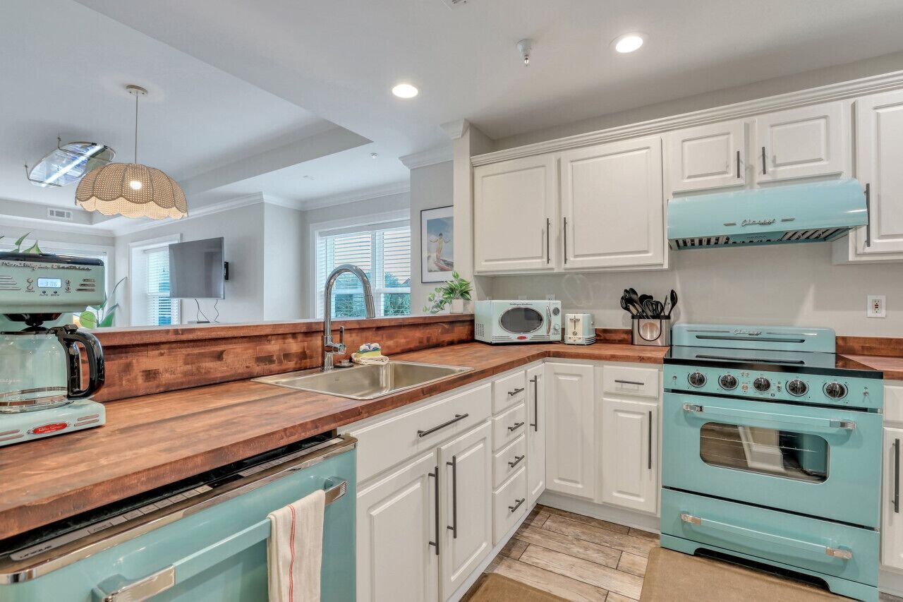 A kitchen with white cabinets, a teal stove, and a wooden countertop.