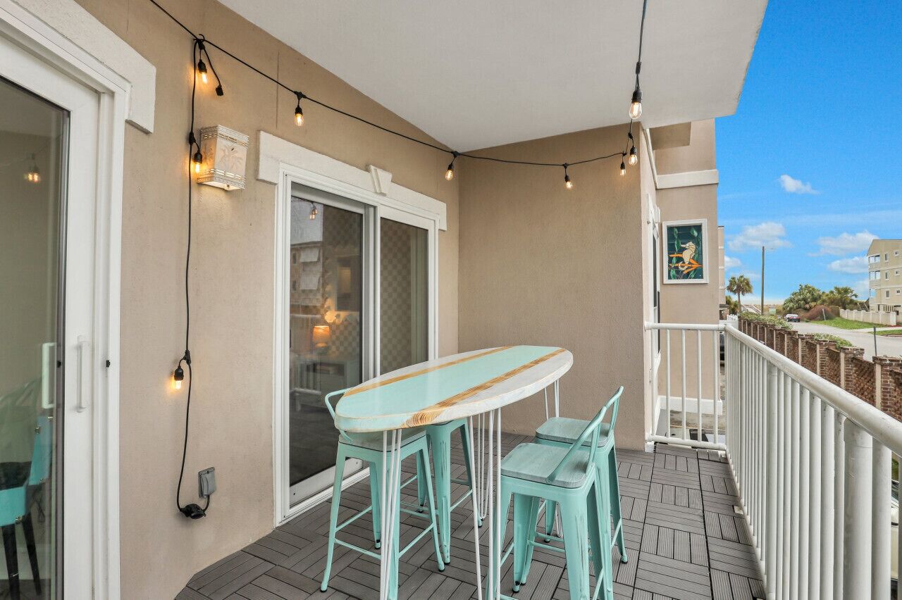A balcony with a table and chairs, string lights, a white railing, and a view of the street.
