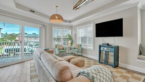 Een ruime woonkamer met een grote bank, een televisie en een balkon met schuifdeuren.