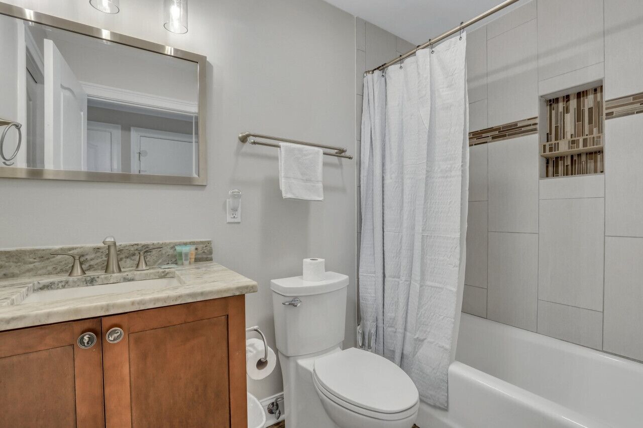 A bathroom with a marble countertop, a wooden vanity, a toilet, a shower with a curtain, and a large mirror.