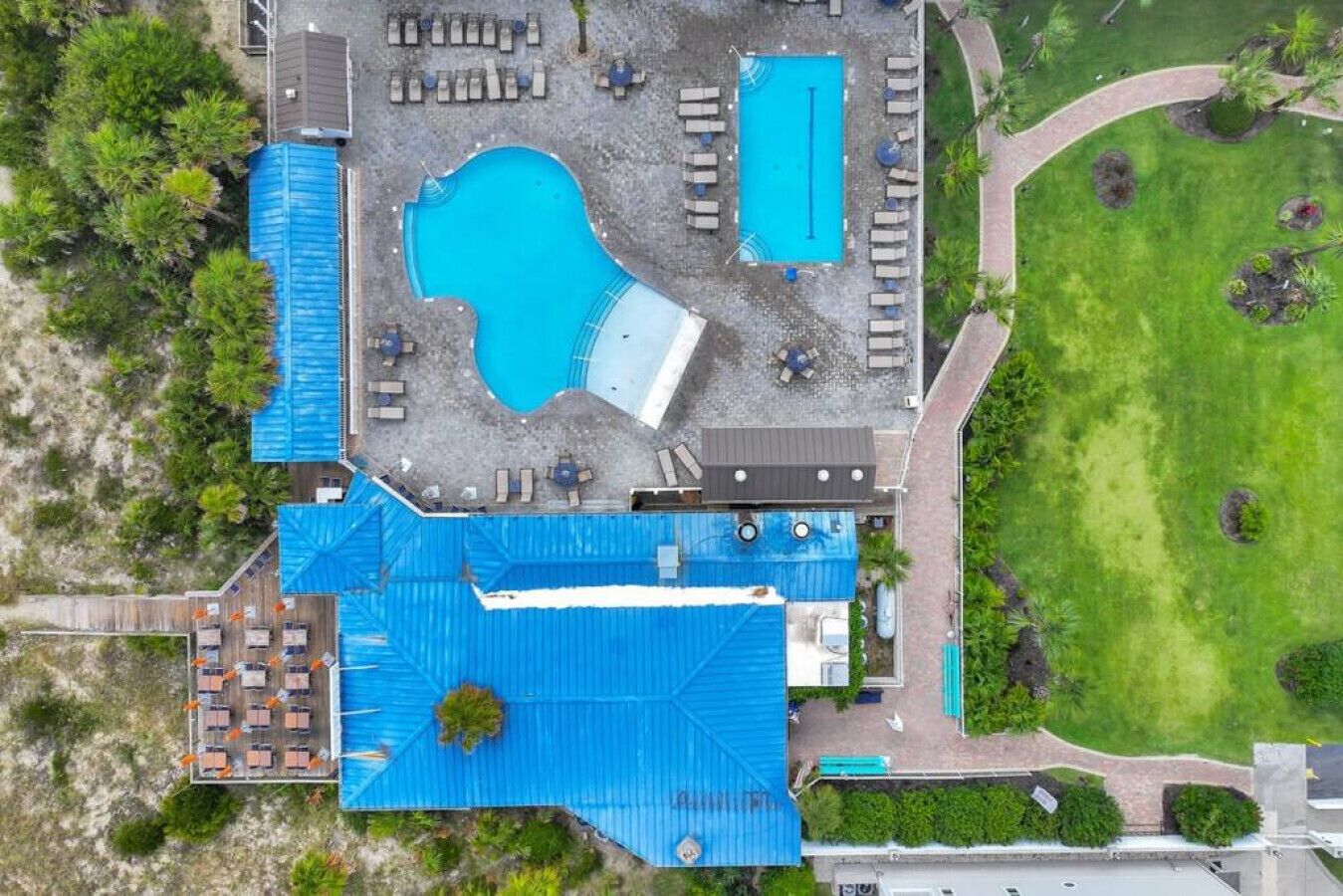 An aerial view of a resort with two swimming pools, a covered patio area, and a well-maintained lawn.