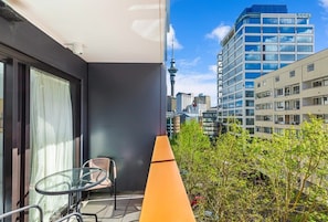 Un balcon avec une table et une chaise en verre, une vue sur le paysage urbain, notamment une tour, et un immeuble doté de balcons.