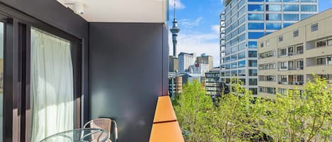 A balcony with a glass table and chair, a yellow chair, and a view of a cityscape including a tower.