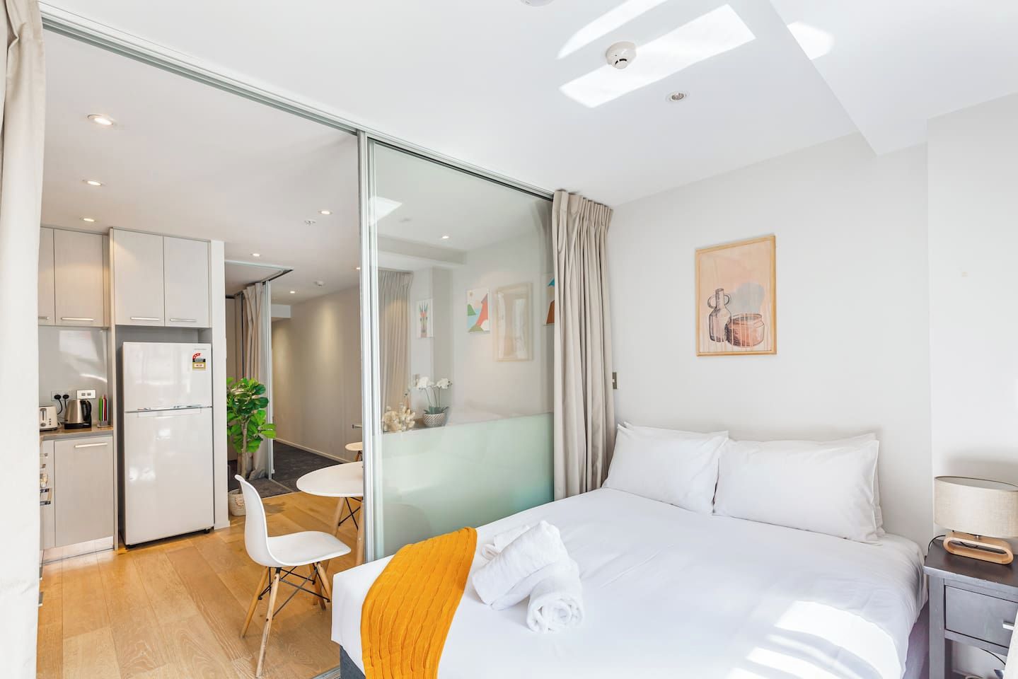 Ein modernes Hotelzimmer mit Bett, Schreibtisch, Stuhl, einer kleinen Küchenzeile und einer Glastür zu einem Essbereich.