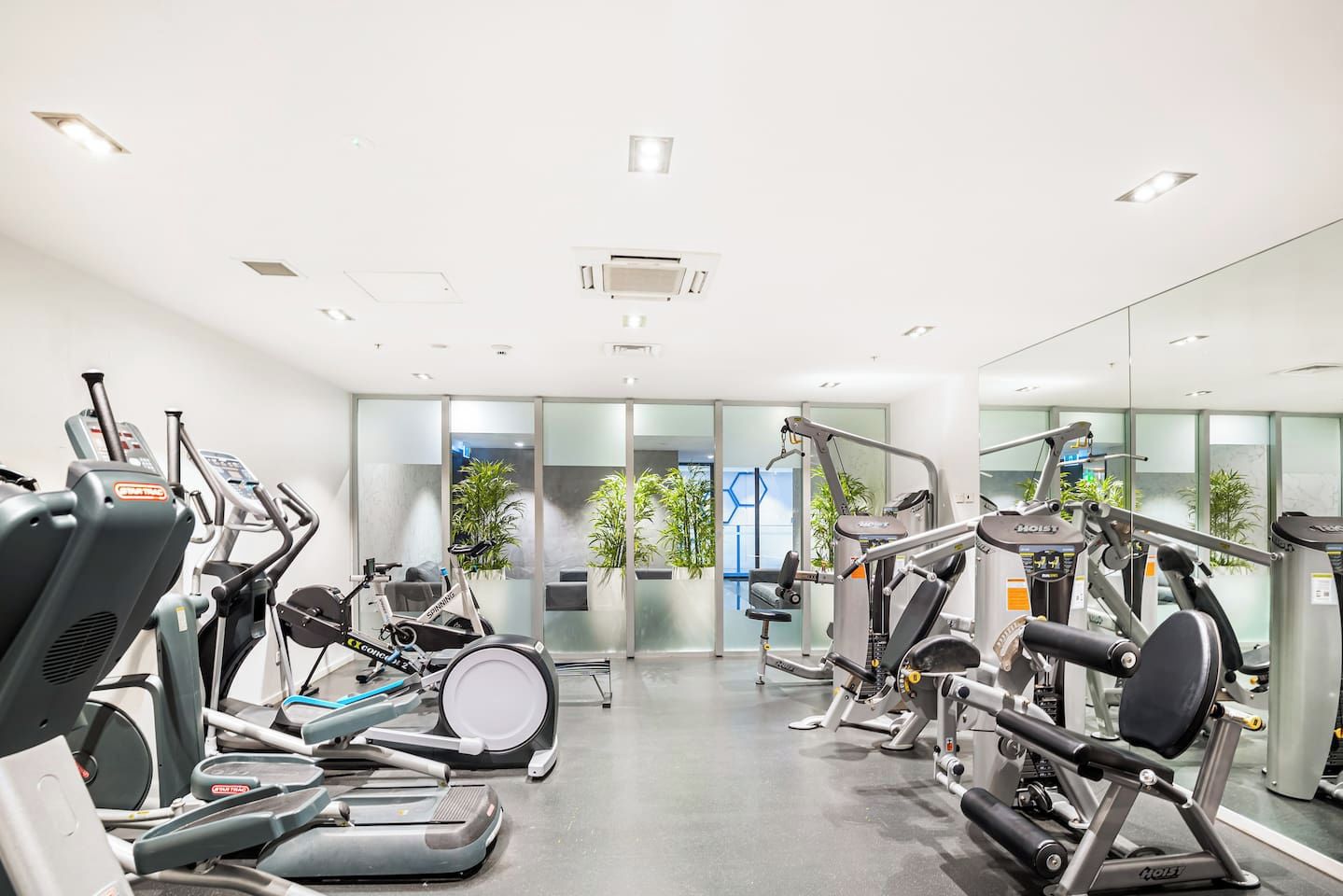 Une salle de sport équipée de divers appareils d’exercice, notamment des tapis de course, des vélos elliptiques et des appareils de musculation.