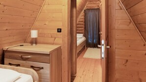 A wooden cabin room with a bed, a desk, and a small window with curtains.