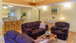 A spacious living room with dark sofas, a coffee table, and a kitchen in the background.