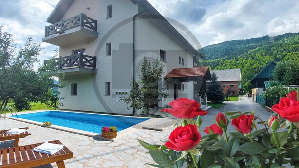 A two-story building with a pool, surrounded by greenery and mountains.