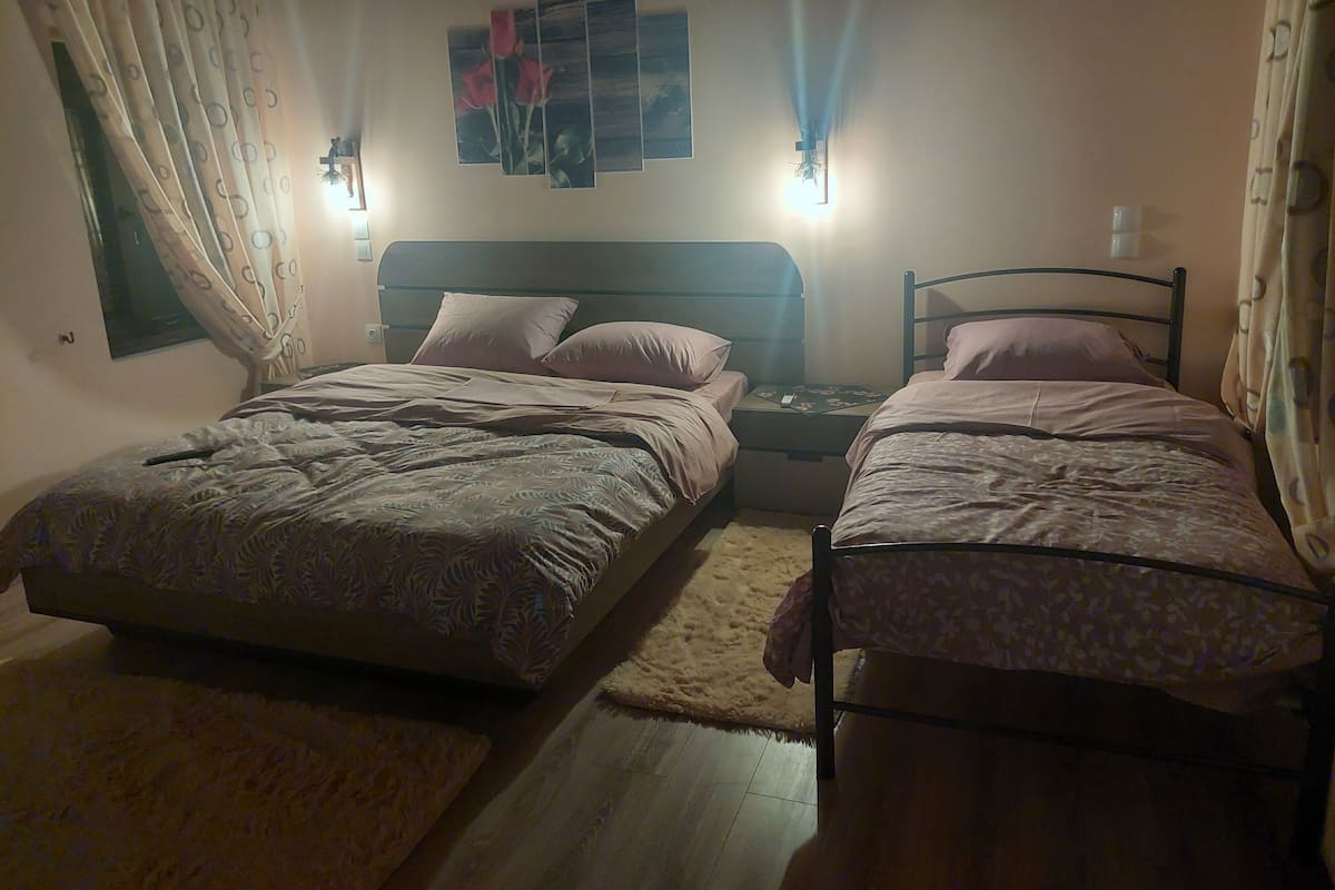 A bedroom with two single beds, a nightstand, a wall-mounted light, and a window with curtains.