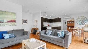A modern living room with two grey sofas, a wooden coffee table, and a dining area with a wooden table and chairs. - Spring Central 29 Centrally Positioned 3 bedroom unit close to shops and beach (Torquay)
