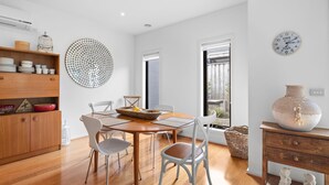 A modern kitchen with wooden cabinets, a dining table with chairs, a large decorative mirror, and a view of the outdoors through a window. - Spring Central 29 Centrally Positioned 3 bedroom unit close to shops and beach (Torquay)