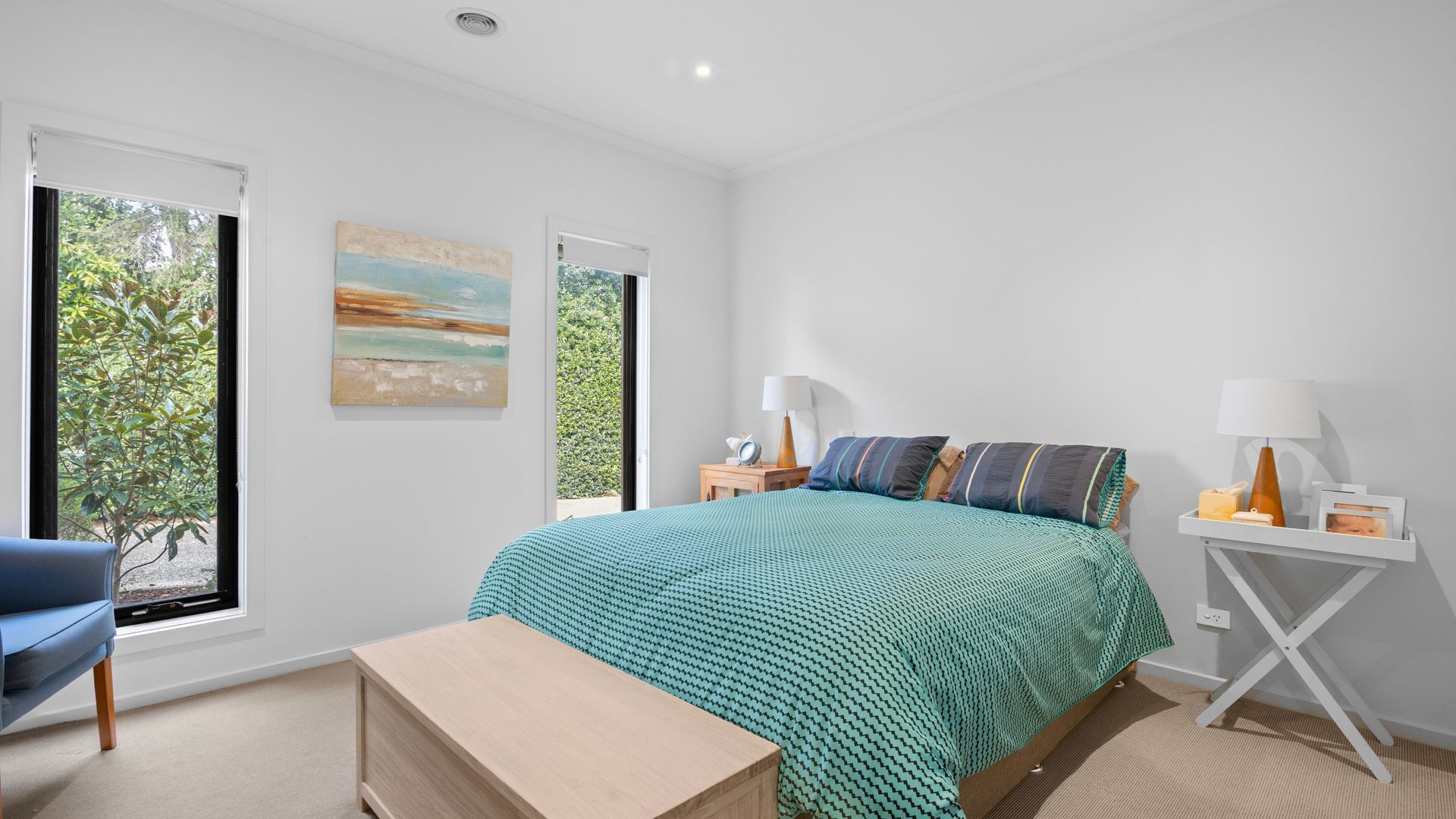 Une chambre à coucher comprenant un lit, deux tables de chevet, une chaise et une fenêtre donnant sur un paysage verdoyant.