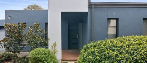 Una casa moderna de dos pisos amb façana gris, una porta d'entrada de fusta i un petit porxo amb una planta en test i un bord.
