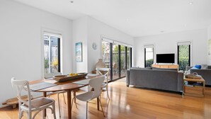 A spacious living area with a wooden floor, a grey sofa, and a dining table with chairs. - Spring Central 29 Centrally Positioned 3 bedroom unit close to shops and beach (Torquay)