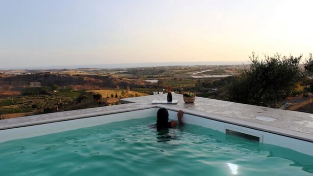 A person relaxing in a pool with a scenic view of a valley and distant buildings. - Modern villa with pool near the Valley of the Temples and the Scala dei Turchi. (Favara)