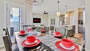 Un coin repas avec une table dressée pour quatre personnes, un ventilateur de plafond et une cuisine en arrière-plan.