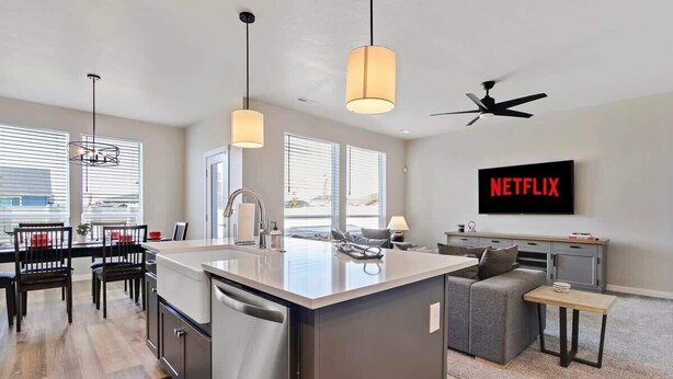 Une cuisine moderne avec un îlot central, un coin repas avec des chaises, un canapé et un téléviseur diffusant du contenu « NETFLIX ».