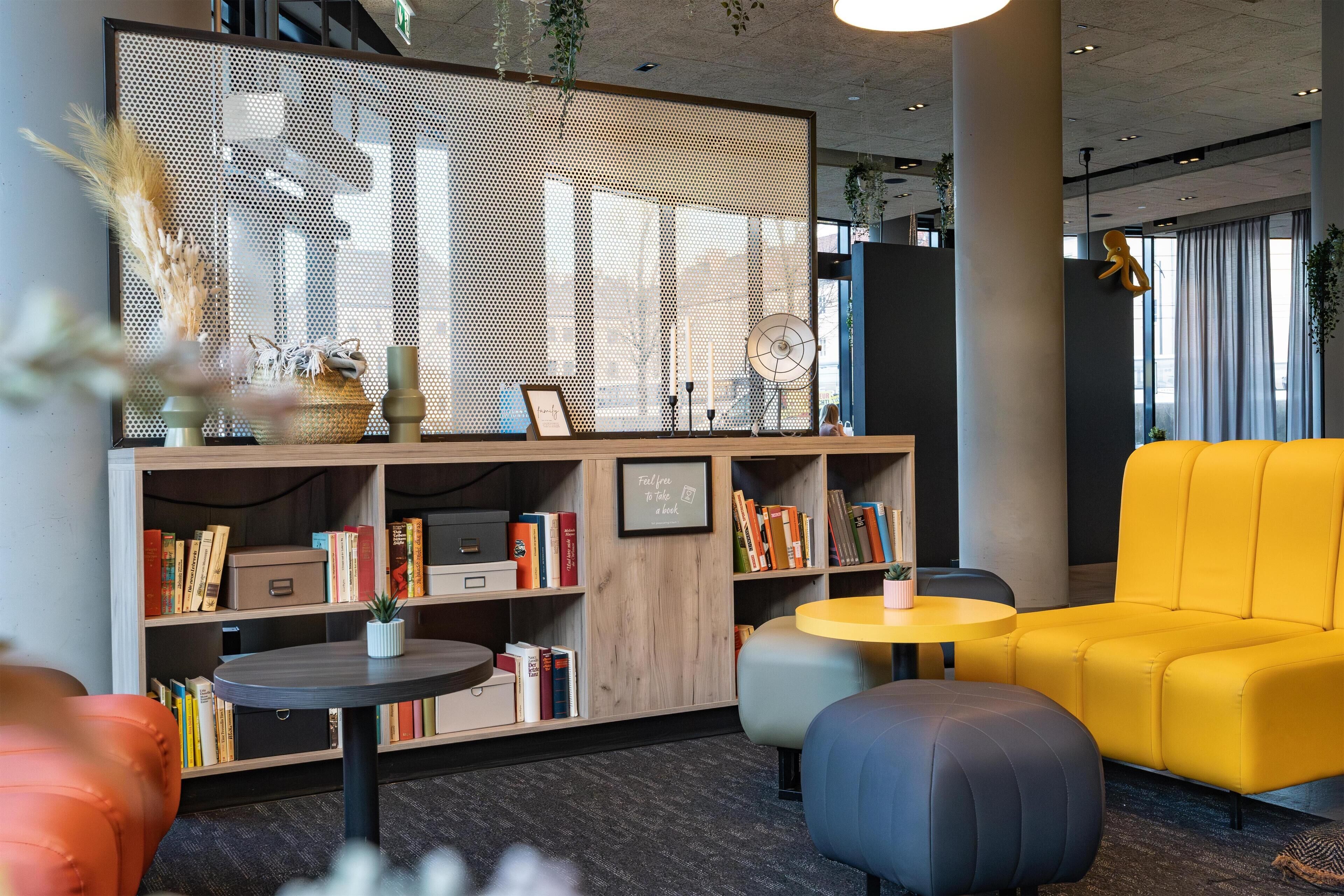 A modern lounge area with a yellow sofa, round tables, and a bookshelf filled with books.
