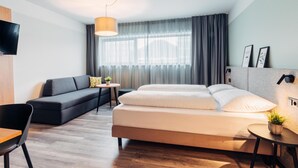 A modern hotel room with a bed, a sofa, a small table, and a TV. - harry's home Salzburg (Salzburg)